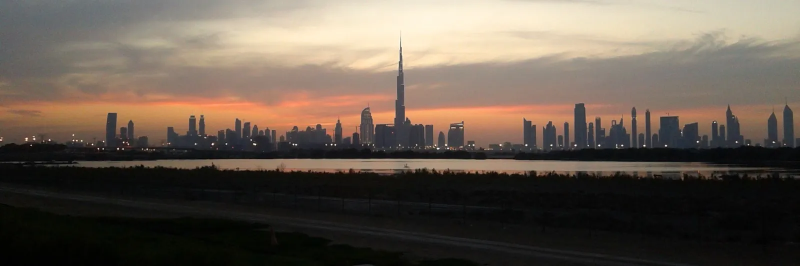 The Dubai skyline at dusk, seen across water from the edge of the city
